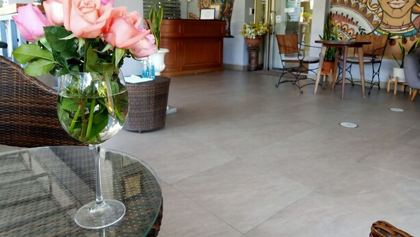 A reception area with a glass vase of pink roses on a table, wicker furniture, and a mural on the wall. - Kavil Guesthouse (Chiang Mai)