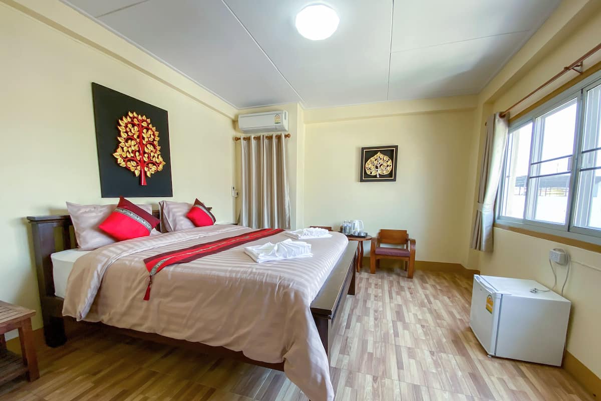 A hotel room with a bed, a small table, a chair, an air conditioning unit, and a window.