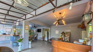 A reception area with a wooden counter, a ceiling fan, and a wall-mounted TV. - Kavil Guesthouse (Chiang Mai)
