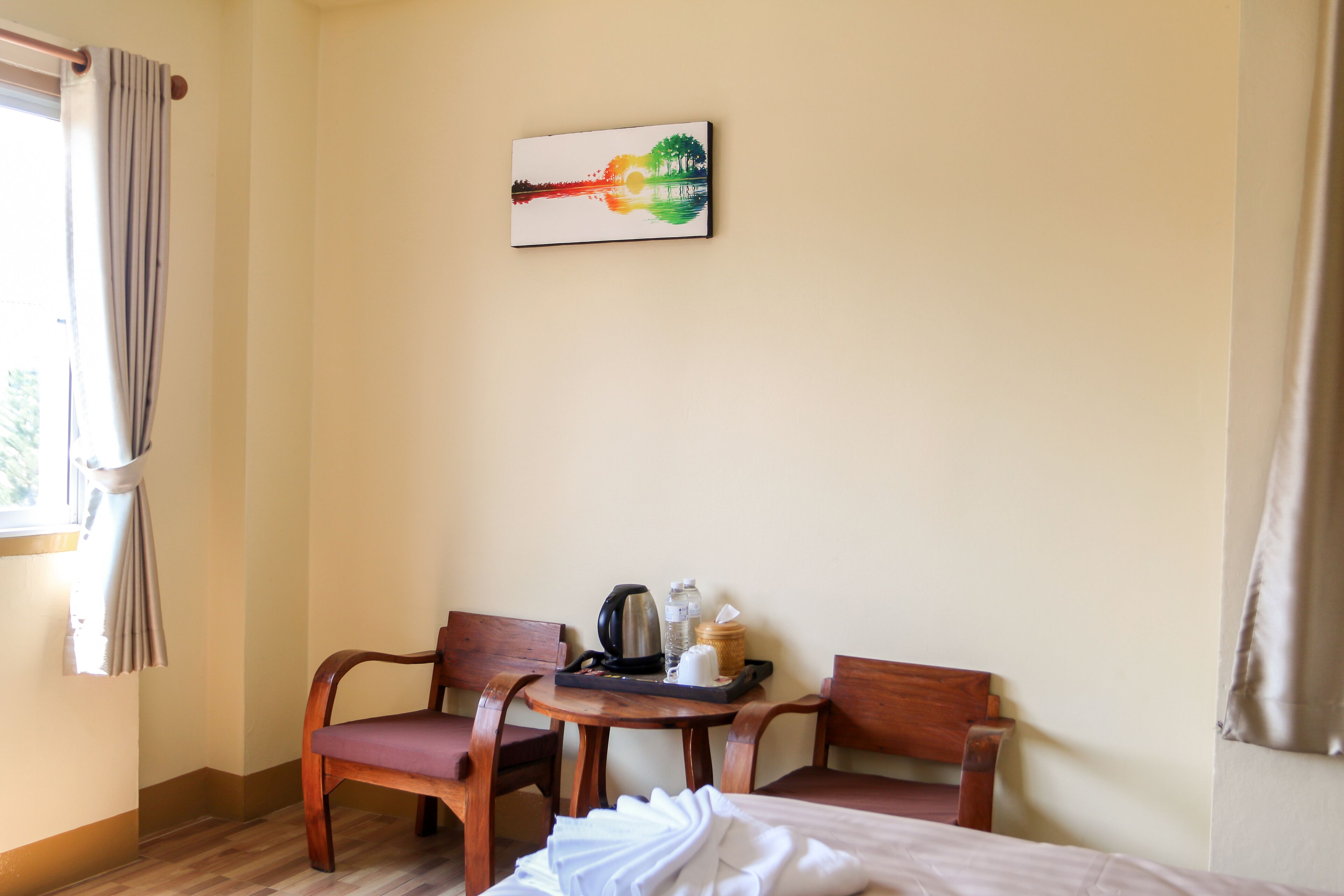 A hotel room with a bed, two wooden chairs, a small round table with a kettle, a bottle, and a tray.