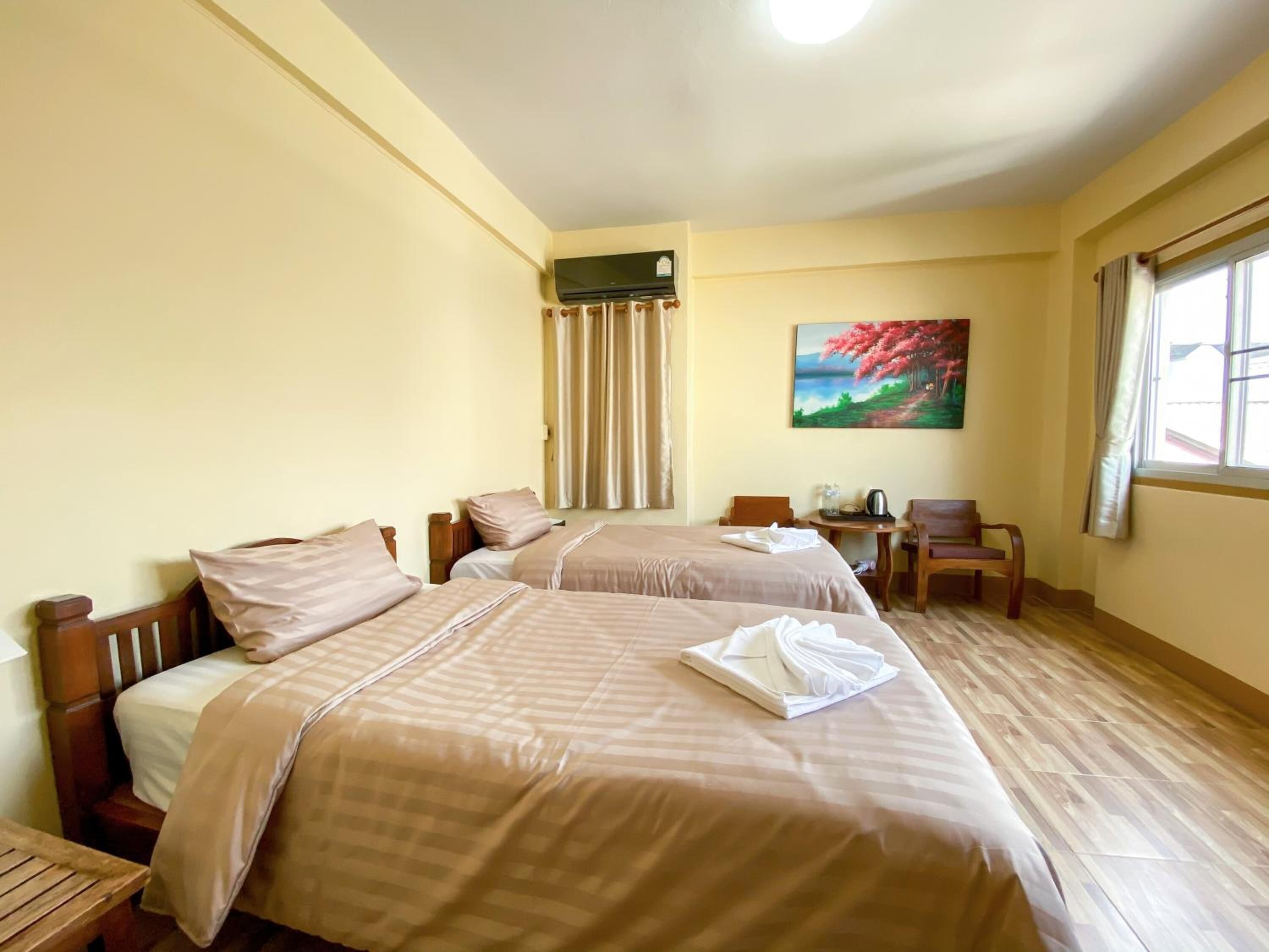 A hotel room with two beds, a painting, a window with curtains, and a small table.