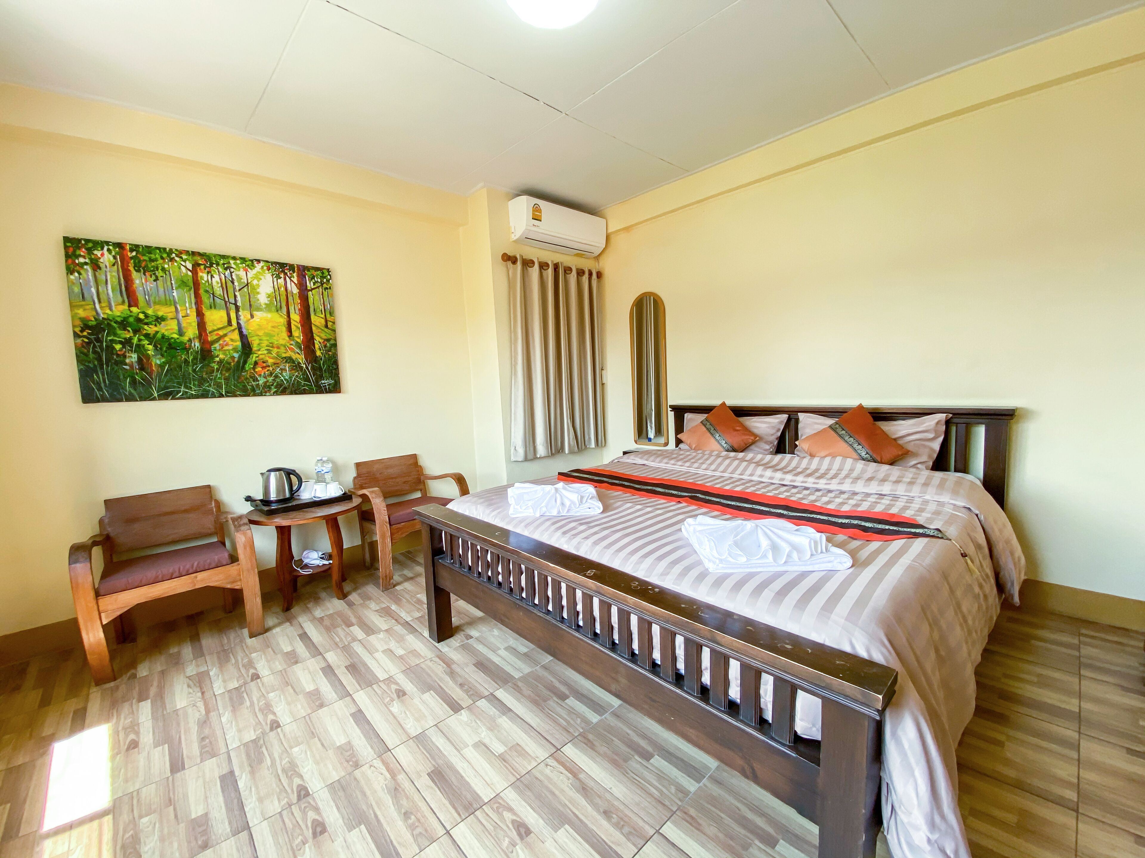 Habitación de hotel con una cama grande, un escritorio con hervidor, sillas y un cuadro de un bosque.
