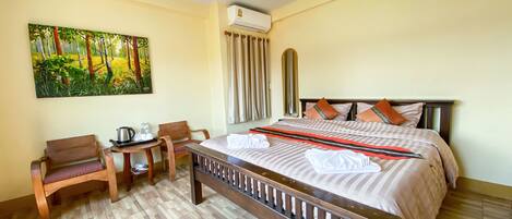 Habitación de hotel con una cama grande, un escritorio con hervidor, sillas y un cuadro de un bosque.