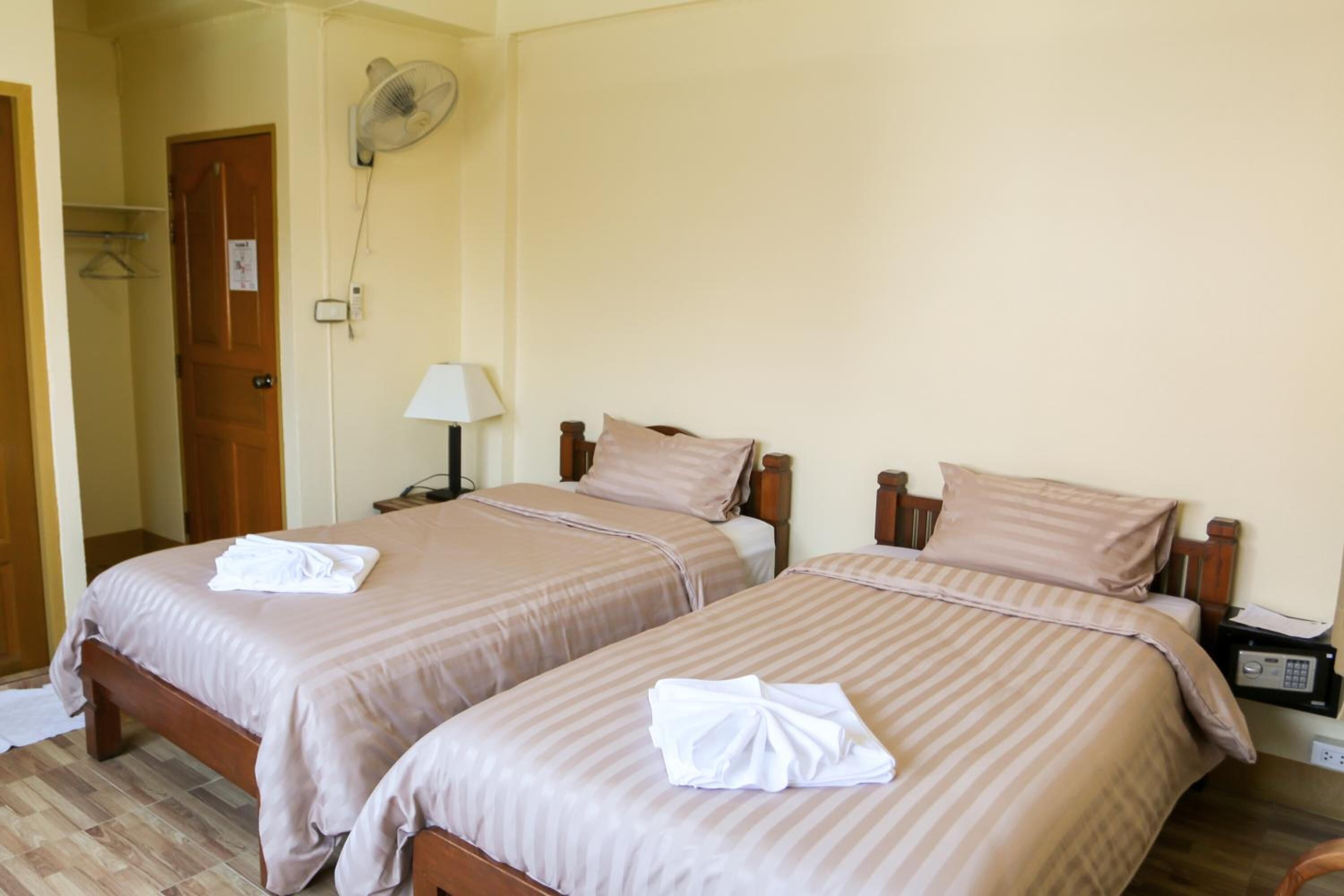Een hotelkamer met twee bedden, een nachtkastje met een lamp, een ventilator aan de muur en een houten deur.