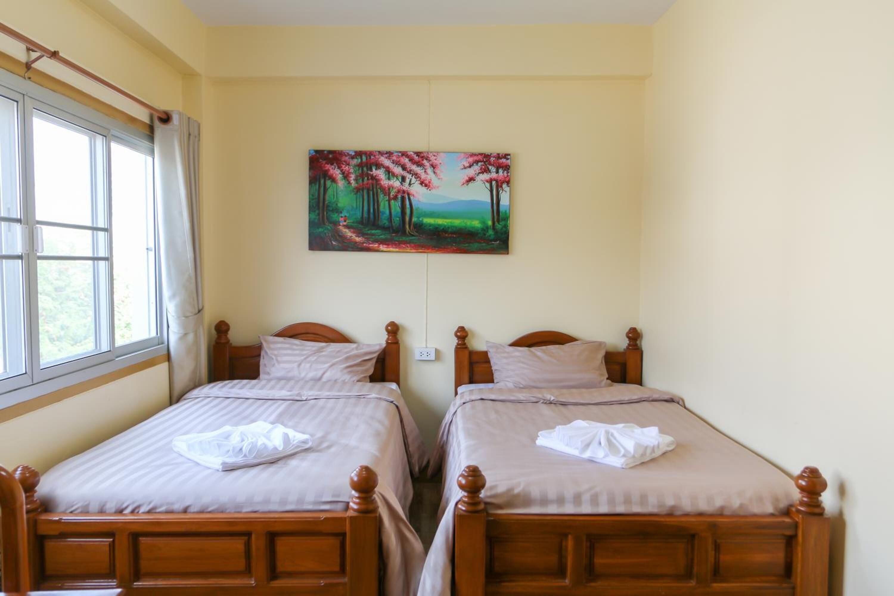 Una habitación de hotel con dos camas de madera, un cuadro de un bosque y una ventana con cortinas.