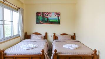 Una habitación de hotel con dos camas de madera, un cuadro de un bosque y una ventana con cortinas.