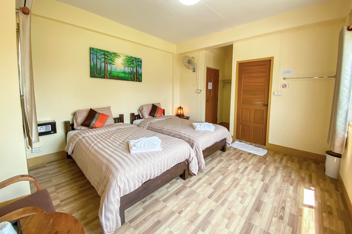 A hotel room with two beds, a painting on the wall, a wooden floor, a door, and a trash bin.