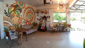 A cozy cafe with a mural, a sofa, tables, and chairs. - Kavil Guesthouse (Chiang Mai)