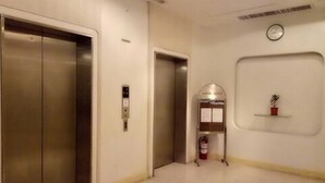 Un pasillo con dos ascensores, un reloj en la pared y una pequeña planta en maceta sobre una estantería.