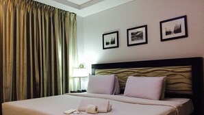 Habitación de hotel con una cama grande, dos almohadas, una mesita de noche con lámpara y tres cuadros enmarcados en la pared.