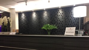 Mostrador de recepción con un fondo negro estampado, un cartel de recepción y una planta en maceta.