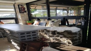 A cozy room with a stone bench, a white bar area, and large windows offering a view of the outdoors. - Starlightdrops Pension (Jeju City)
