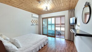 A bedroom with a wooden ceiling, a bed with white bedding, a TV on a shelf, and a sliding glass door leading to a balcony. - Starlightdrops Pension (Jeju City)