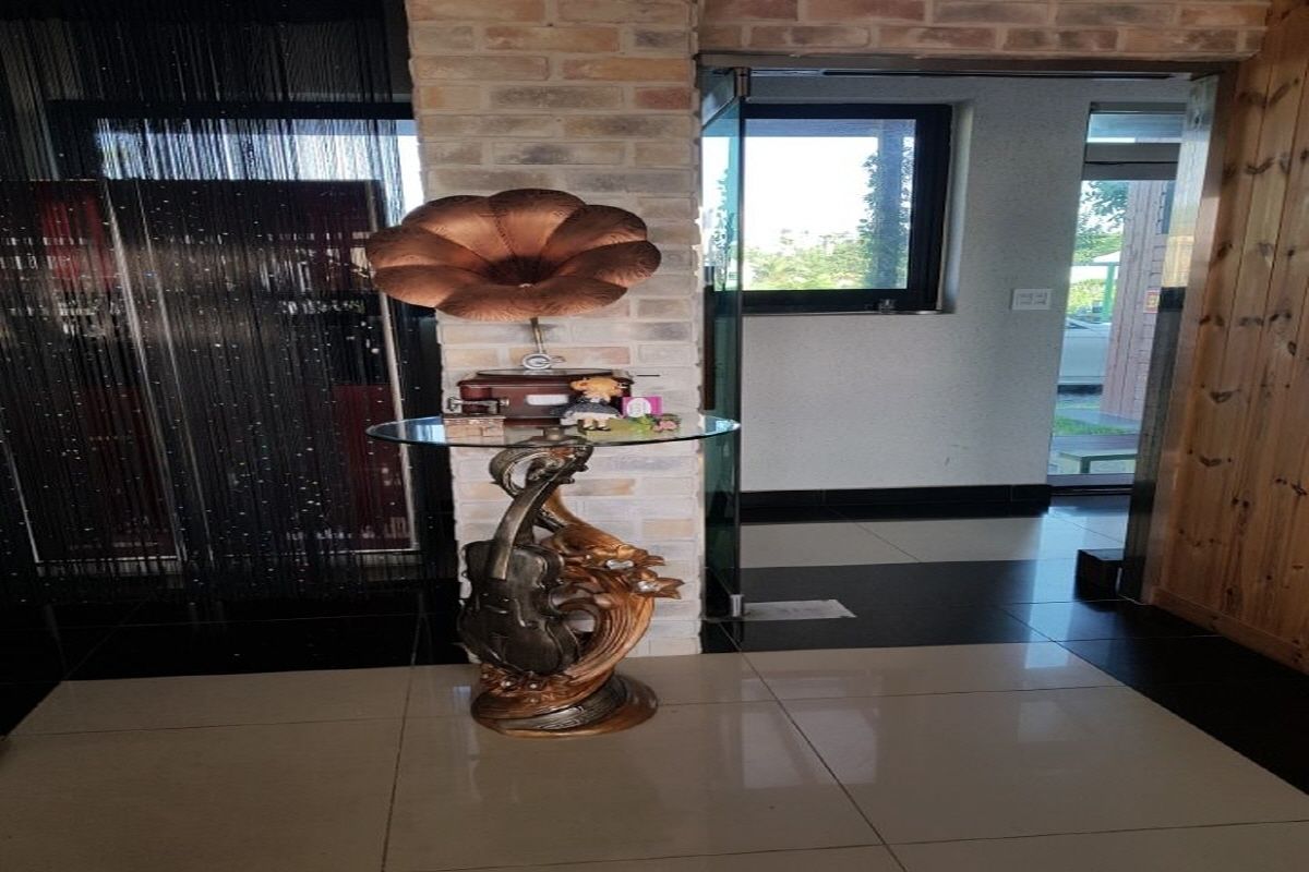 Quarto com mesa de vidro, exibindo uma escultura metálica decorativa, parede de tijolos e janela com vista para o exterior.