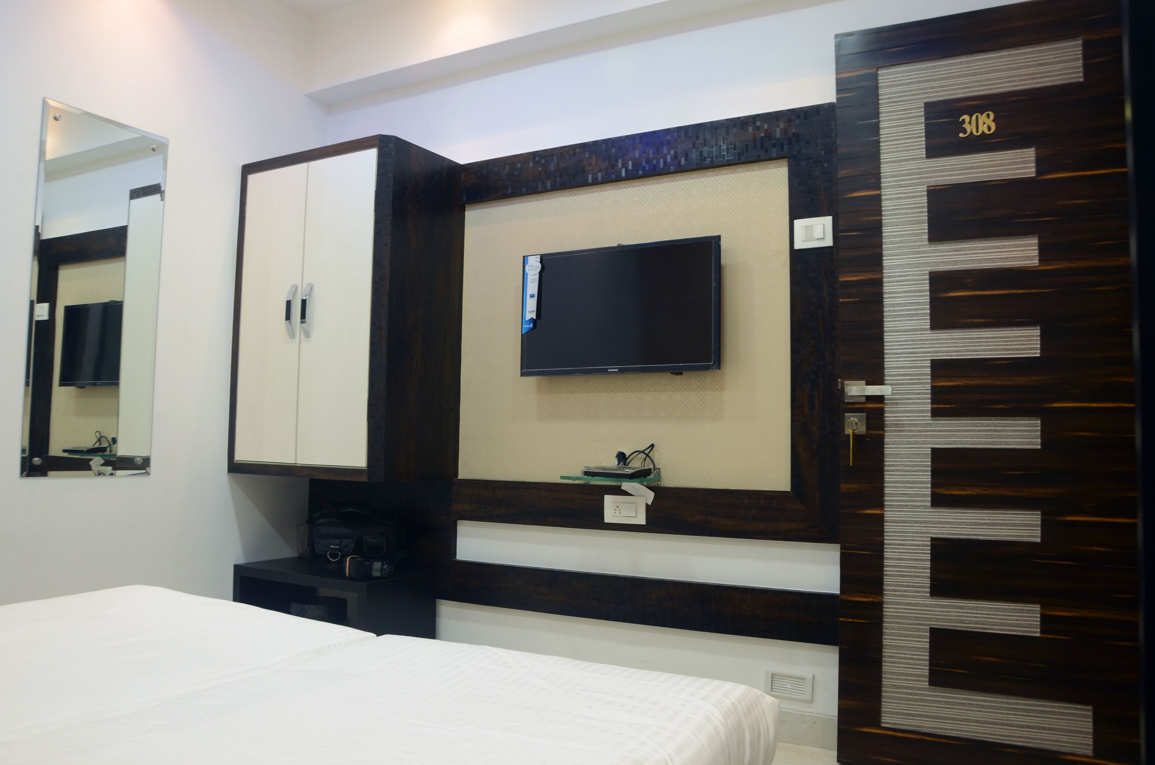 Habitación de hotel con cama, armario, televisor montado en la pared y puerta con el número 308.