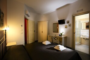 A hotel room with a bed, a desk, a chair, a TV, and a bathroom visible through an open door. - Triskell Camere & Relax (San Vito Lo Capo)
