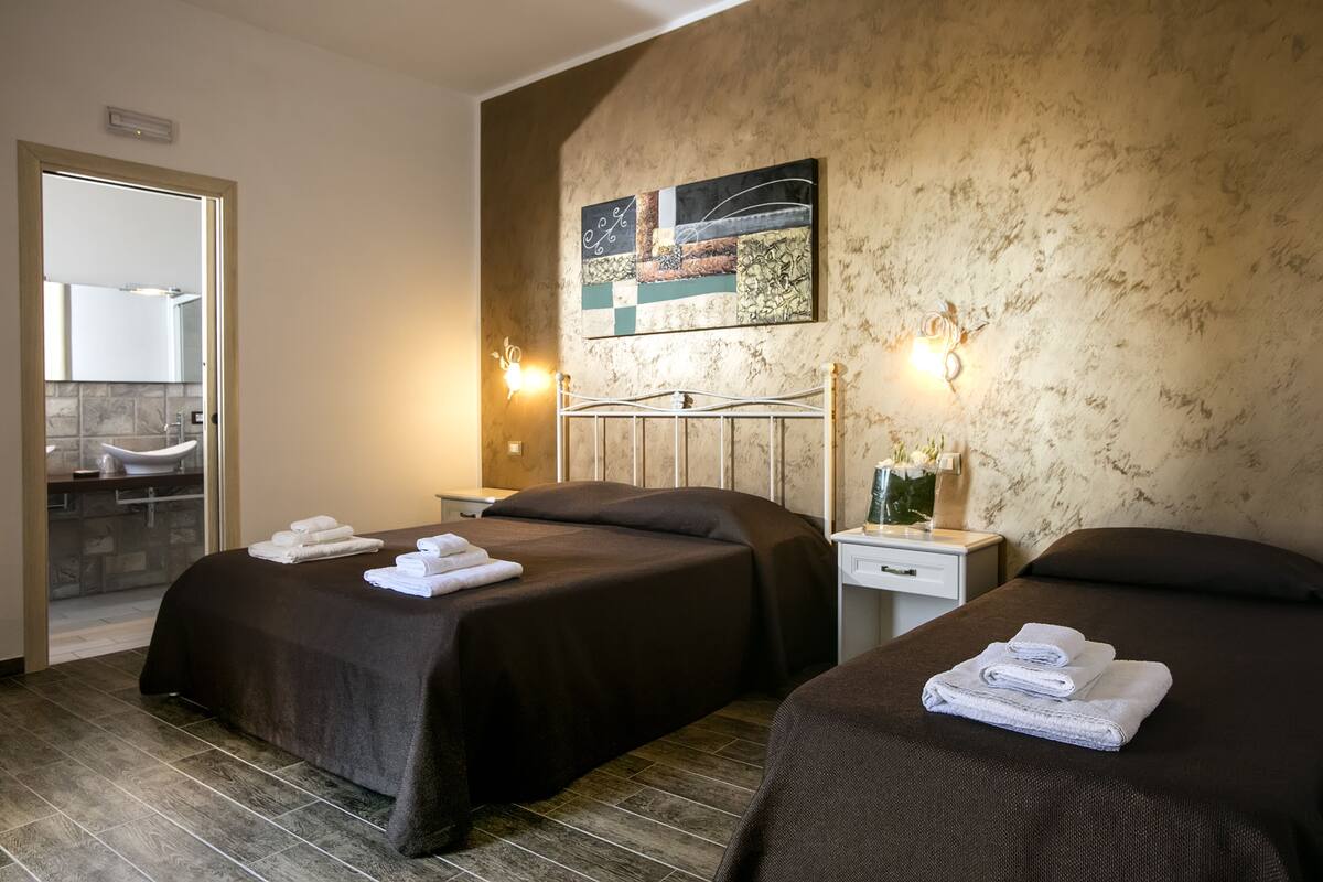 Habitación de hotel con dos camas, un baño con un espejo grande y un cuadro en la pared.