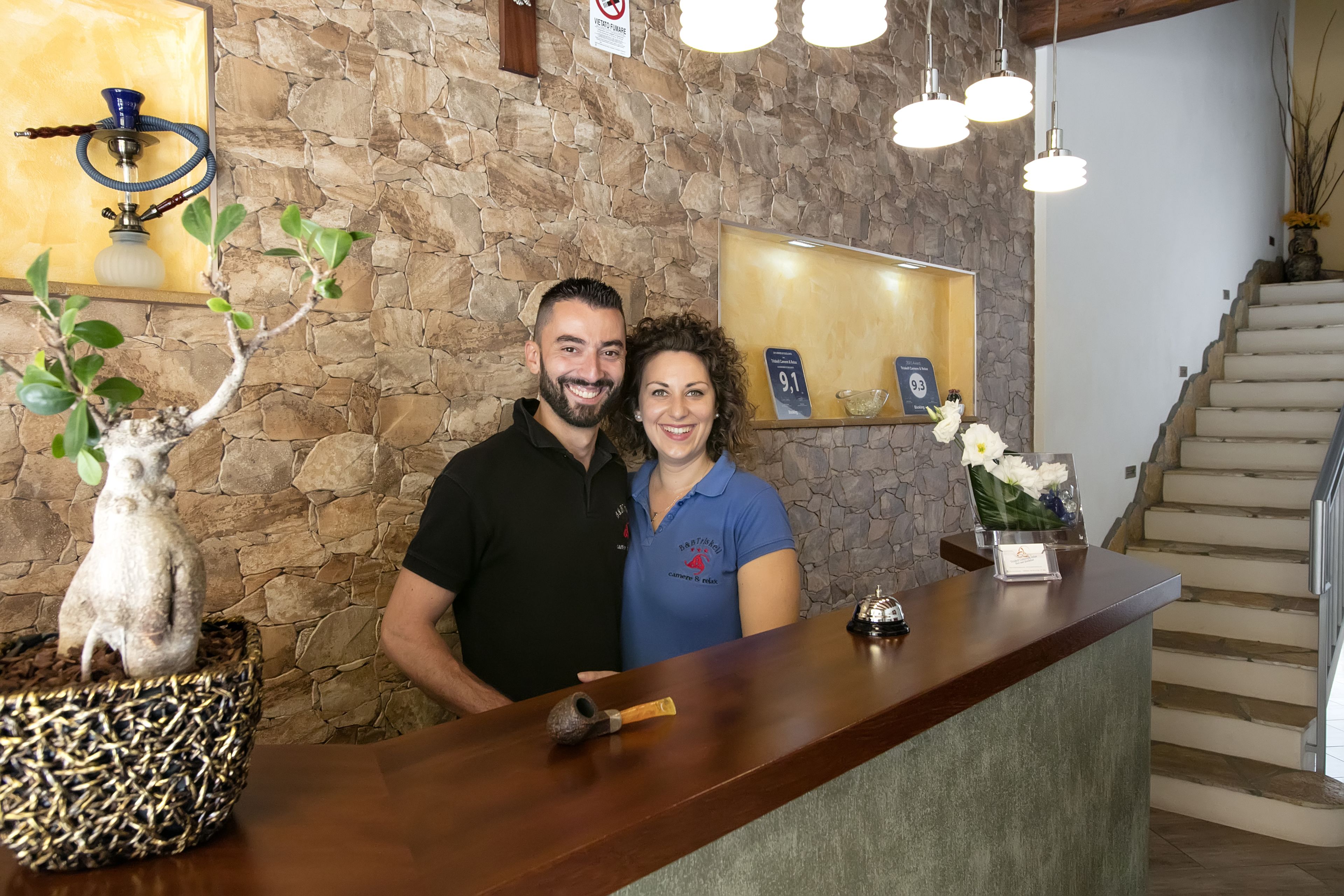 Egy előtér, melyben kőfal, egy fa recepciós pult, egy vízipipa és egy kis, virágcserepes növény található.