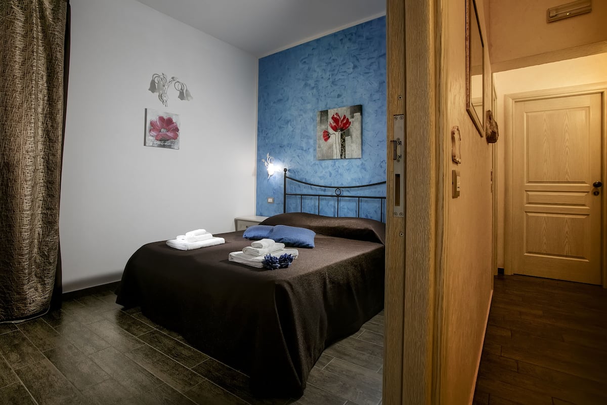 Un dormitorio con cama, mesita de noche, un reloj de pared y una puerta.
