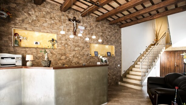 A reception area with a stone wall, wooden ceiling beams, a reception desk, a staircase, and a leather sofa. - Triskell Camere & Relax (San Vito Lo Capo)