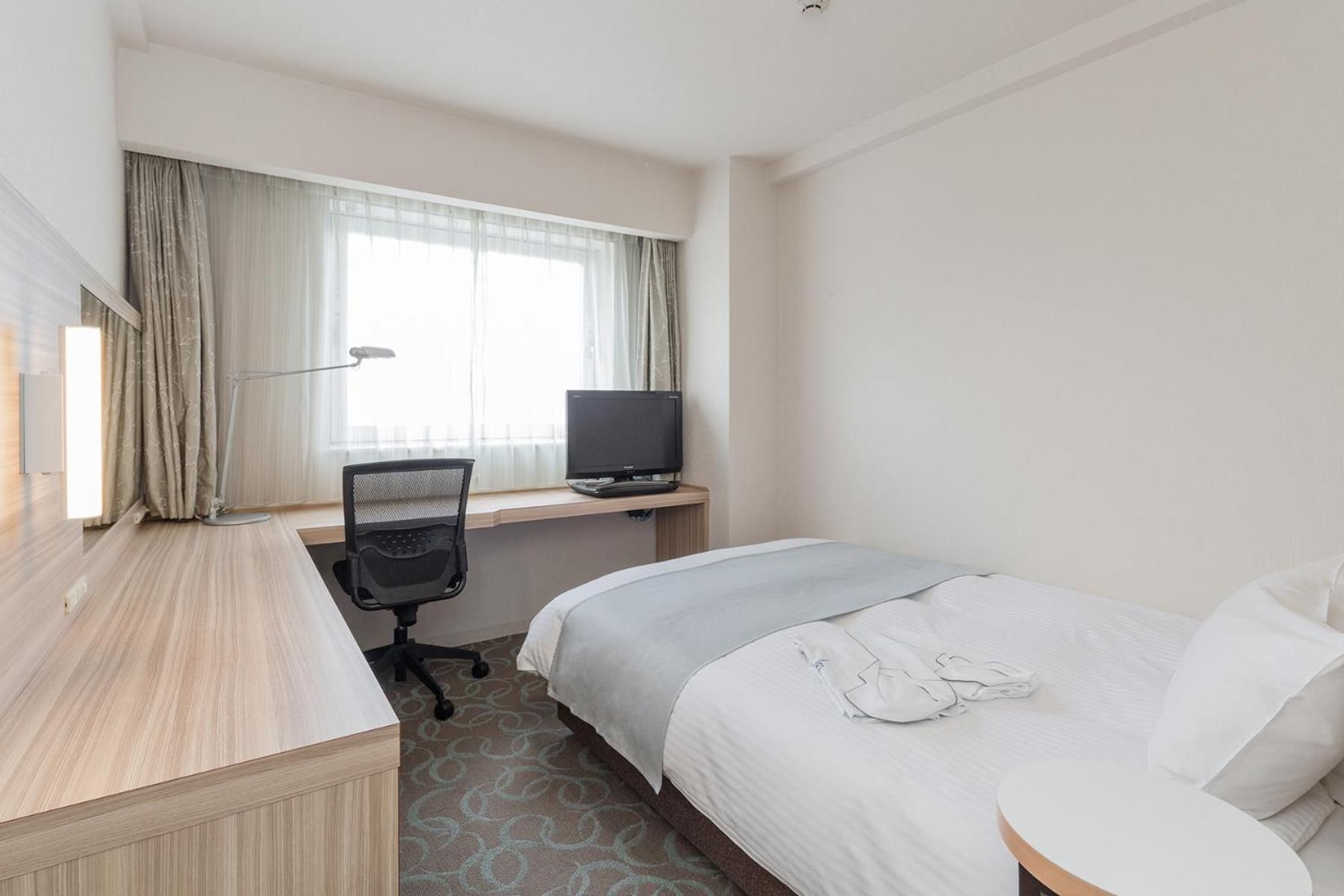 A hotel room with a bed, a desk with a computer, a chair, and a television.