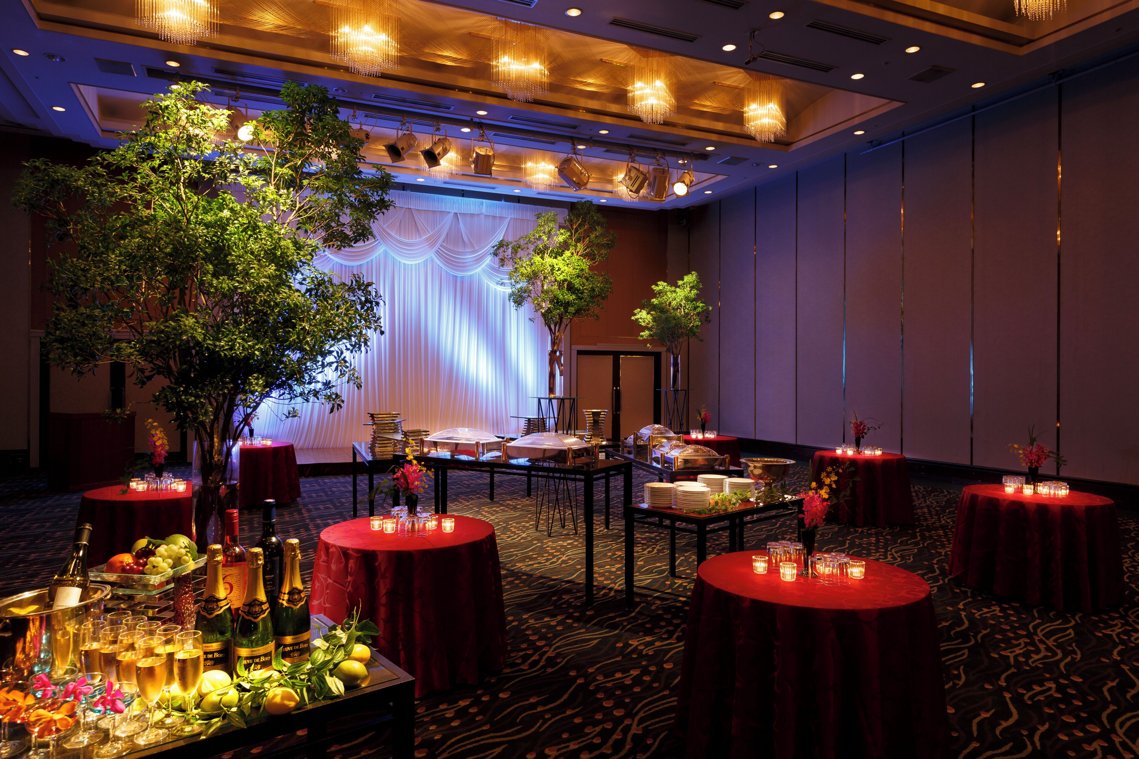 A banquet hall with round tables, a stage with drapes, and a large tree.