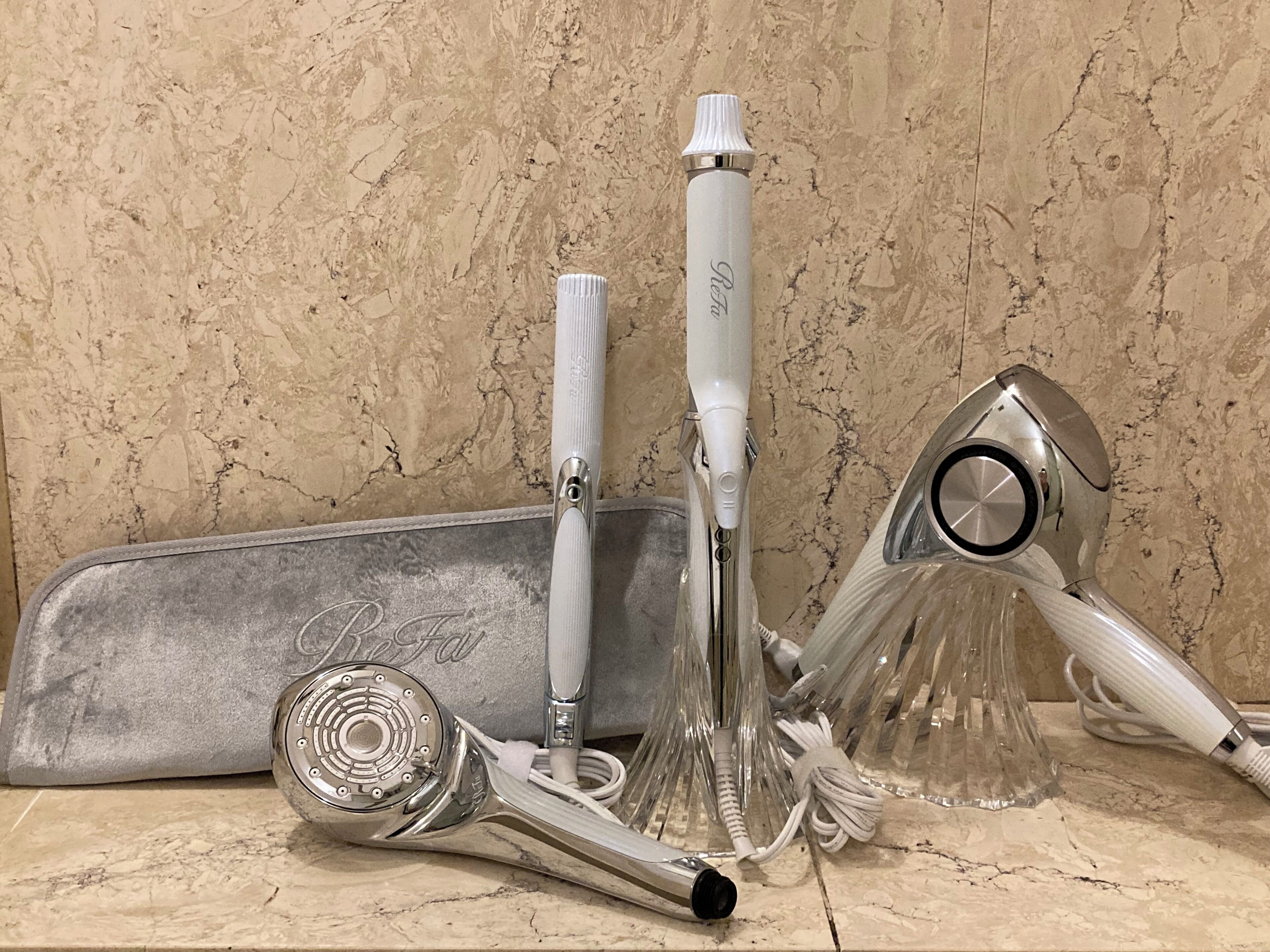 Un baño con encimera de mármol, un afeitador eléctrico plateado, un cepillo de dientes eléctrico blanco y un secador de pelo.