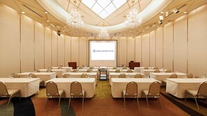 Une salle de conférence équipée de tables, de chaises, d’un écran de projection et de lustres.