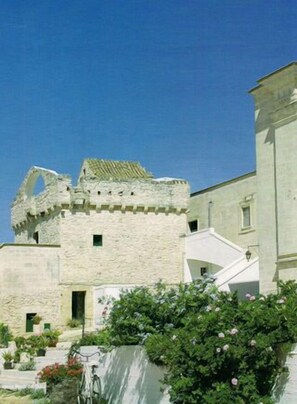 A stone building with a tower, surrounded by greenery and a bicycle. - L'antico Trullo (Fasano)