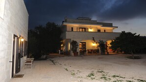 A modern two-story house with a covered patio area, outdoor seating, and a well-lit entrance. - L'antico Trullo (Fasano)