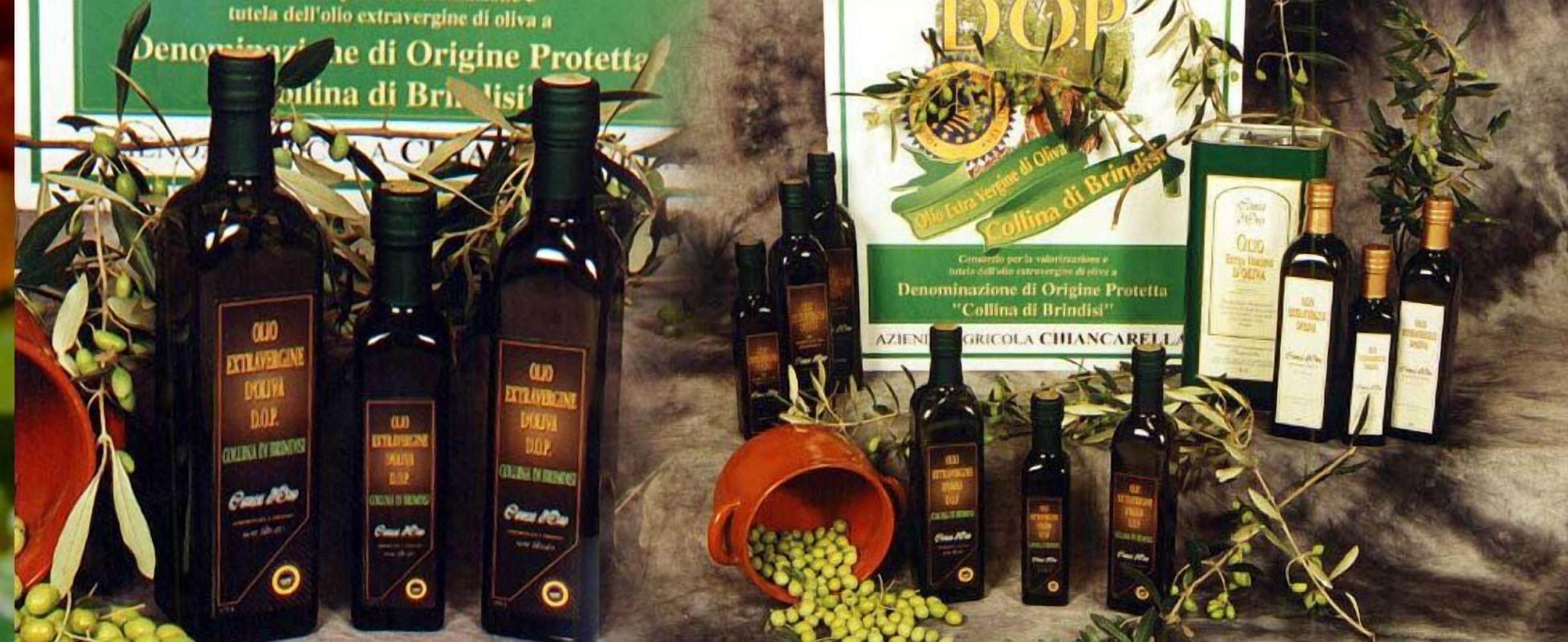 Several bottles of olive oil with labels, some olive branches, and a green sign with text.
