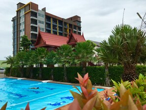Un hotel con piscina, palmeras y un edificio de varios pisos con balcones.