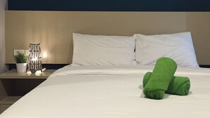 A neatly made bed with white linens, a green towel, and a bedside table with a lamp and a potted plant. - Huahin Terminal (Hua Hin)