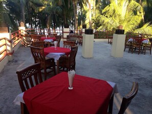 An outdoor dining area with tables and chairs, surrounded by palm trees and a concrete floor. - Kyaw Myanmar Hotel (Ngapali)