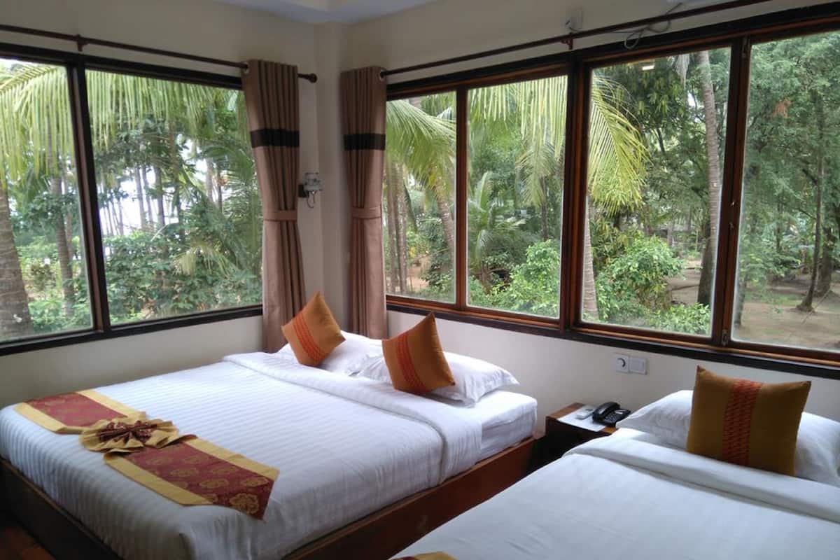 A hotel room with two beds, large windows, and a view of greenery.