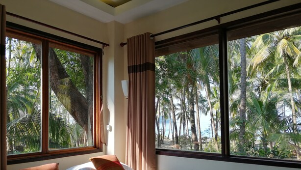 Ein Hotelzimmer mit Bett, Kissen und Blick auf Palmen und das Meer.