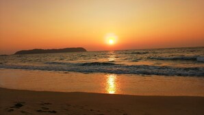 Ein Sonnenuntergang über einem Strand mit Wellen und einer entfernten Landmasse.