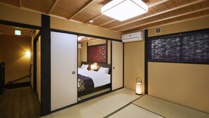 A traditional Japanese-style room with tatami flooring, a bed with white bedding, a lantern, and a view of trees through a shoji screen.
