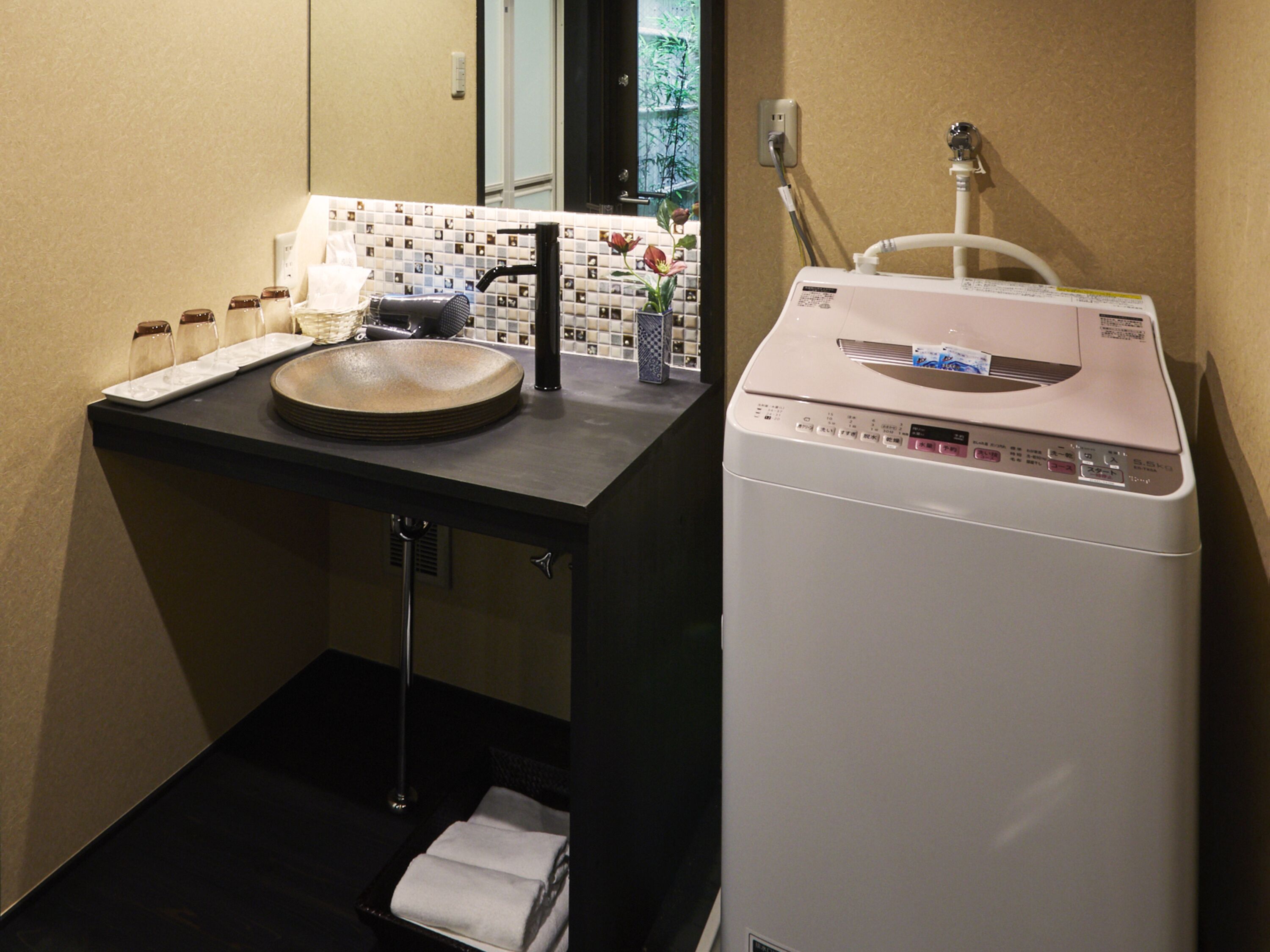 A compact bathroom with a sink, mirror, and a white washing machine.