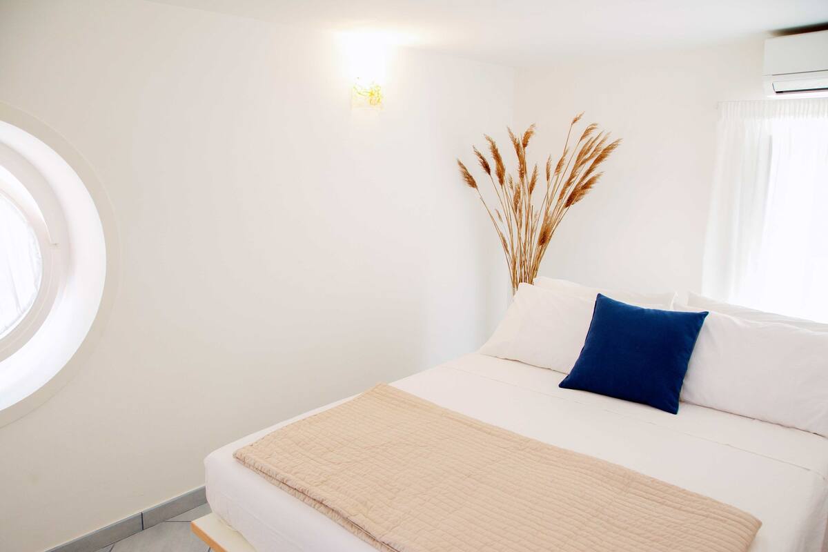 Une chambre à coucher bien rangée, avec un lit, une table de chevet, une fenêtre et un climatiseur fixé au mur.