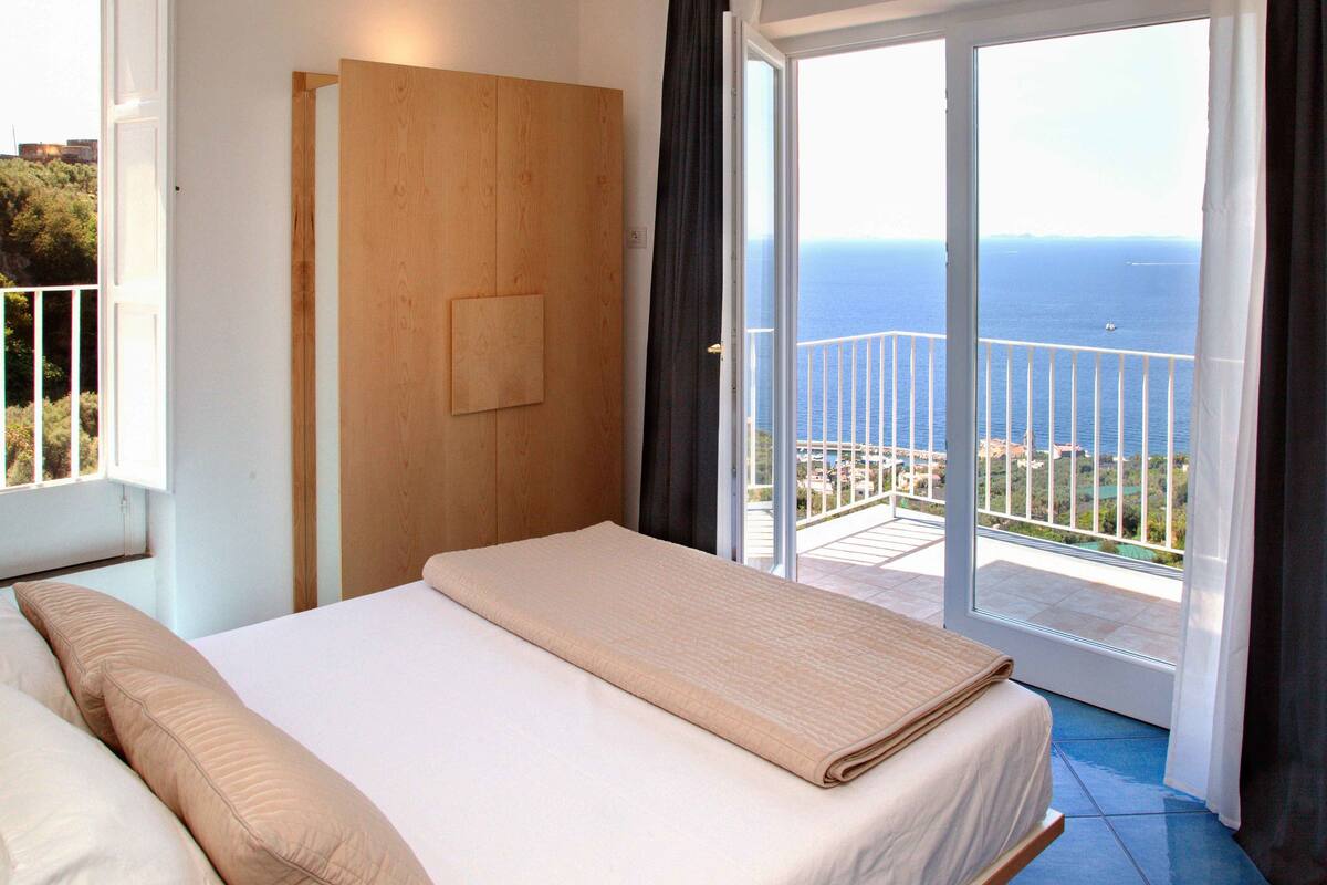 Une chambre avec un lit, une armoire en bois et un balcon donnant sur la mer.