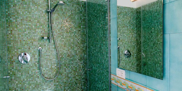 Ein Badezimmer mit mosaikverkleideten Wänden, einer Dusche mit Duschbrause und einem großen Spiegel.