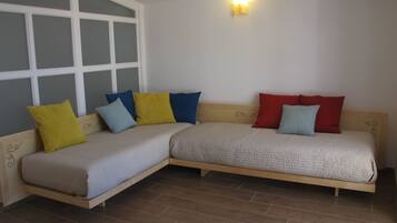 Una habitación con un ventanal grande, una cama con muchos almohadones y una lámpara fijada a la pared.