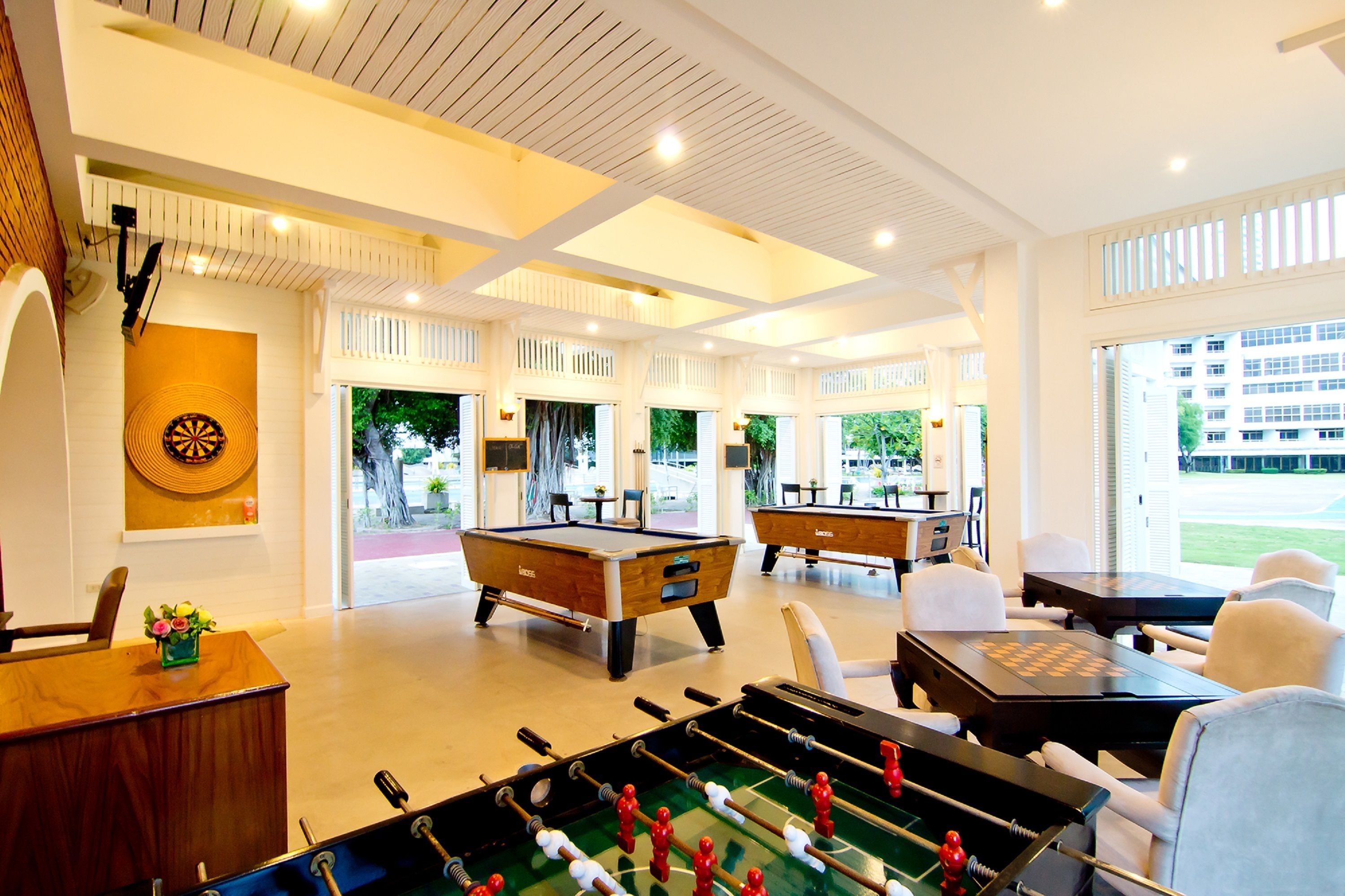 Un vaste espace de loisirs intérieur comprenant des tables de billard, un baby-foot et des sièges confortables.
