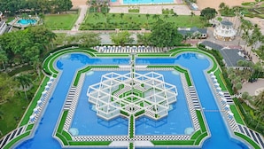 A large, geometrically designed swimming pool with a central hexagonal structure, surrounded by a well-manicured lawn and palm trees. - Ambassador City Jomtien Pattaya - Marina Tower Wing (Sattahip)