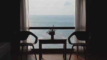 A room with a view of the sea, two chairs, a small table, and a potted plant.