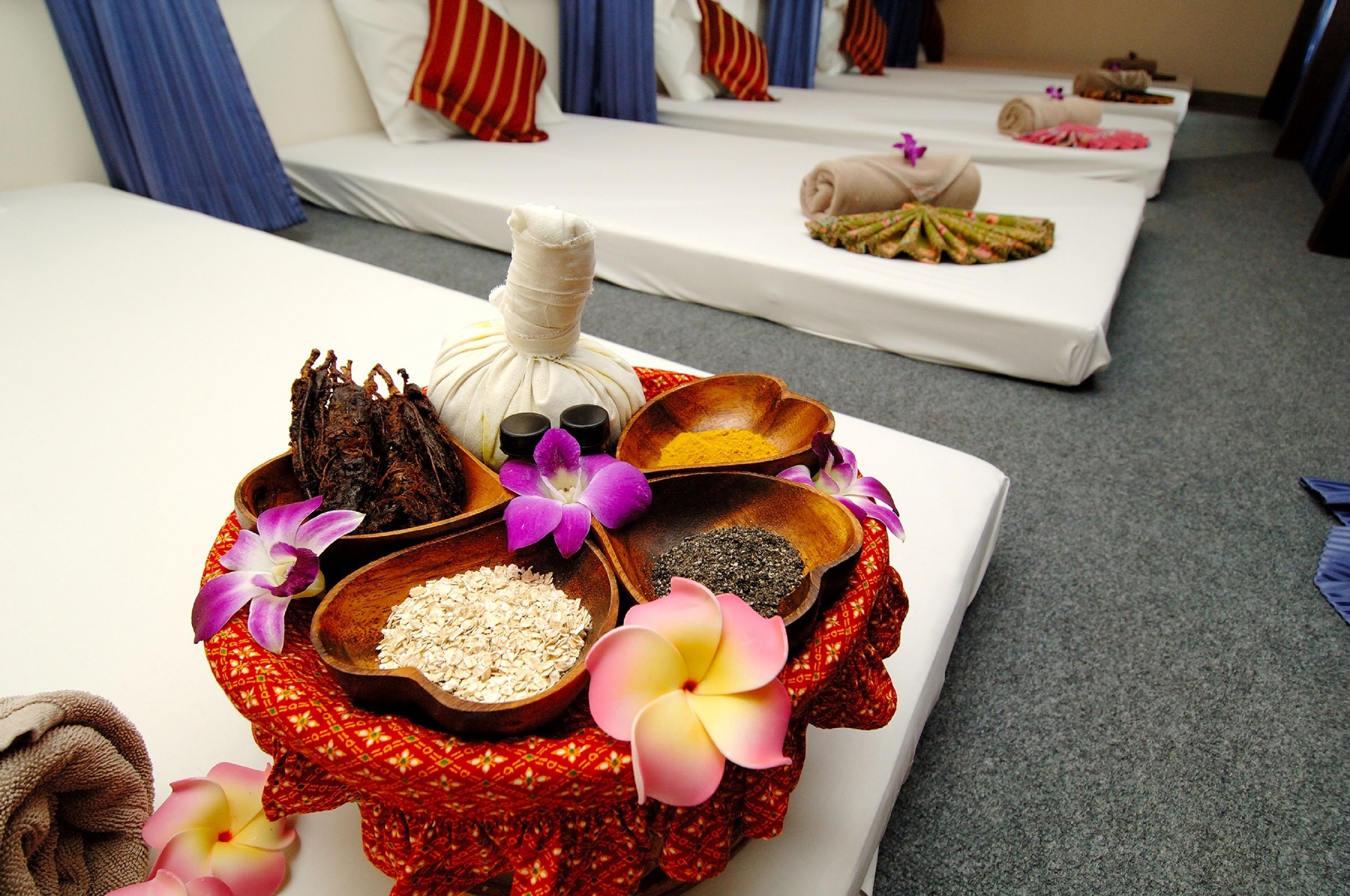 A spa room with multiple beds, a massage table, and a variety of spa products including oils, salts, and flowers.