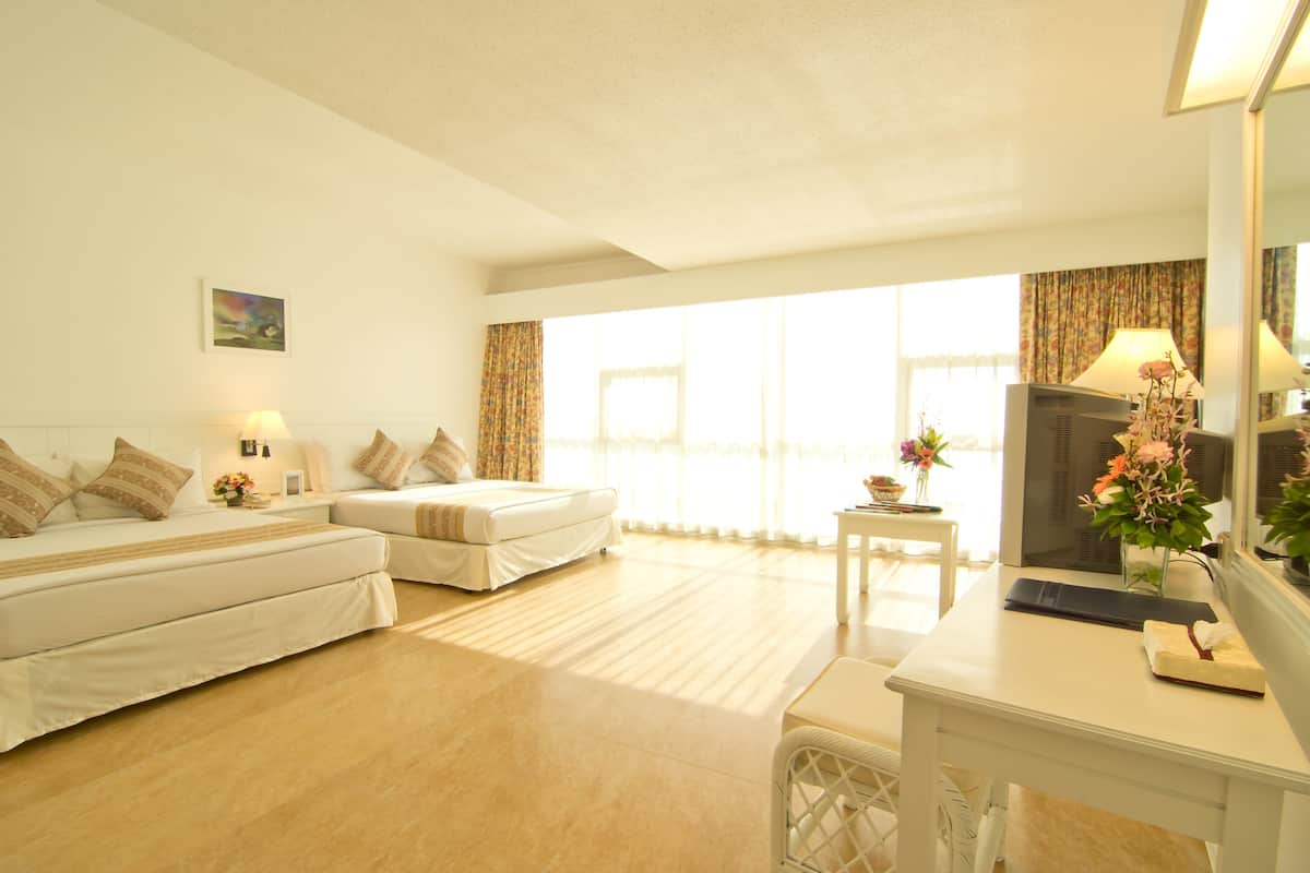 A hotel room with two beds, a desk, a TV, and a window with curtains.