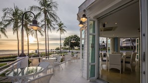 A balcony with white wicker furniture and a glass table, overlooking a beach and palm trees during sunset. - Ambassador City Jomtien Pattaya - Marina Tower Wing (Sattahip)