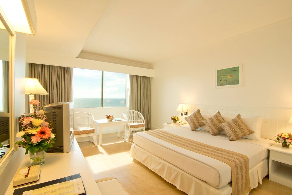 A hotel room with a large bed, a desk with a chair, a TV, and a window with curtains.